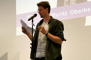Moritz Oberberg beim Poetry Slam des DGB auf der Bühne vorm Mikrofon mit Text in der Hand